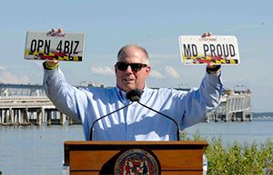 Governor Hogan holding license plates that read MD Proud and OPN 4BZ